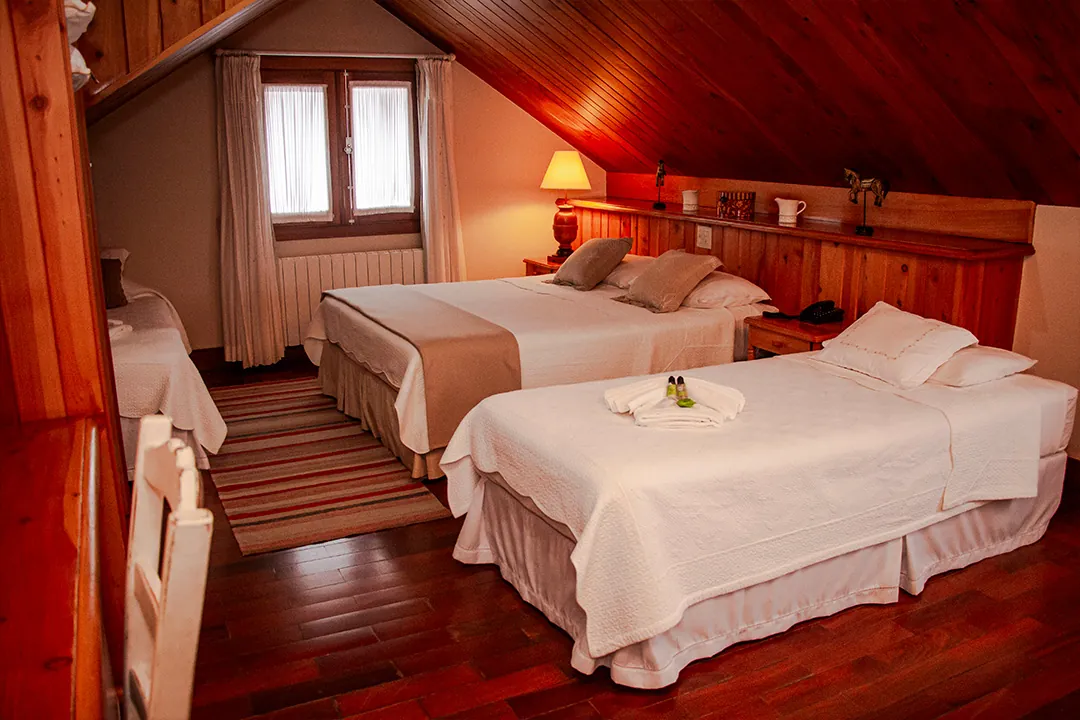 Quarto sótão de madeira com duas camas e luminária acesa
